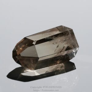 Close-up of a faceted smoky quartz crystal resting on a reflective surface.