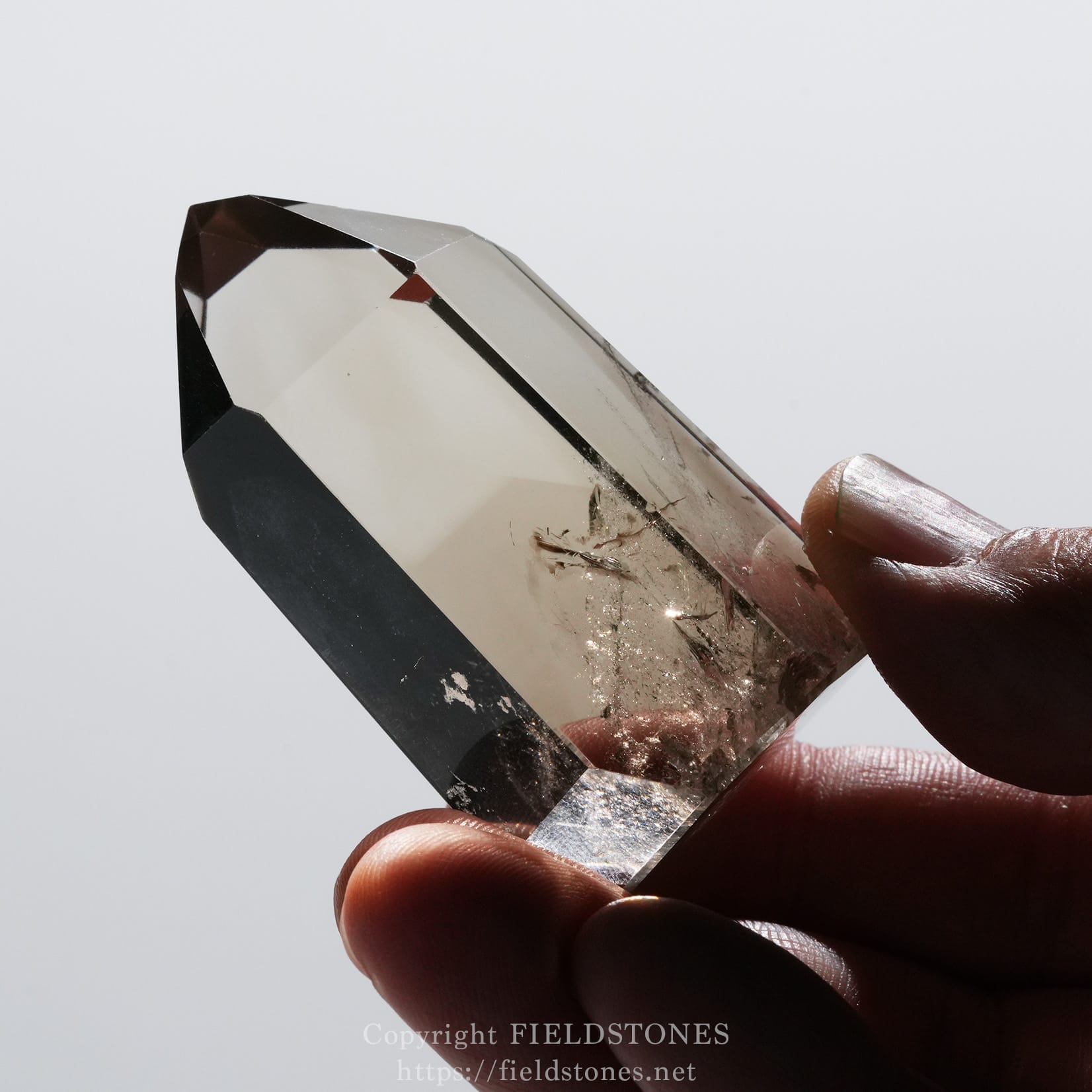 6709-10 - FieldStones Close-up of a large faceted crystal being held between fingers against a light background.