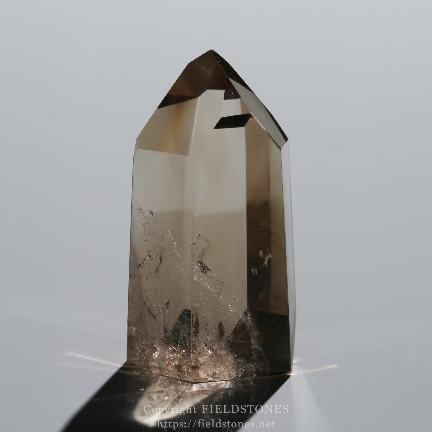 6709-4 - FieldStones Close-up of a tall smoky quartz crystal with a pointed tip, set against a neutral background.