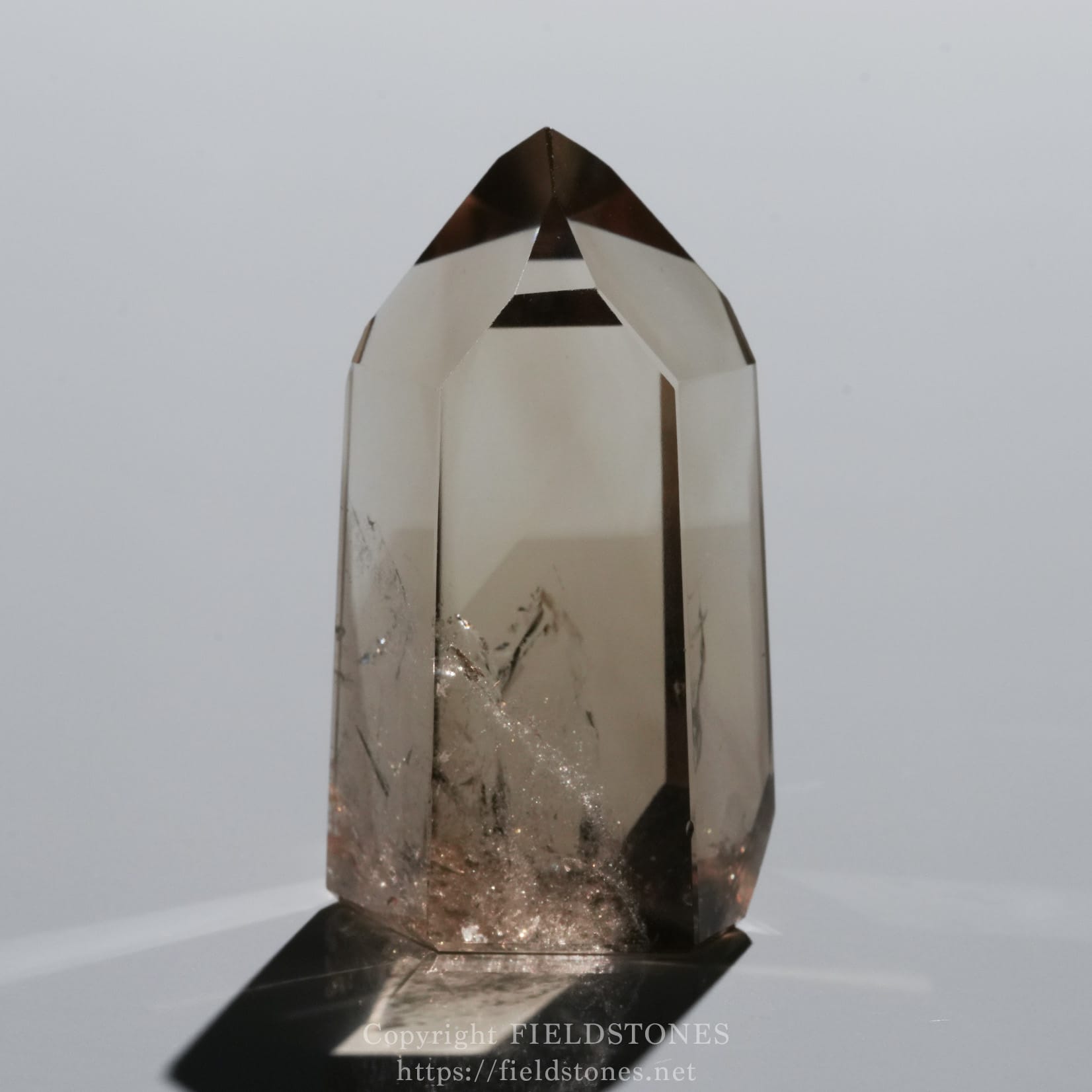6709-5 - FieldStones Tall faceted crystal obelisk with a pointed tip, smoky quartz color resting on a black base against a pale background.