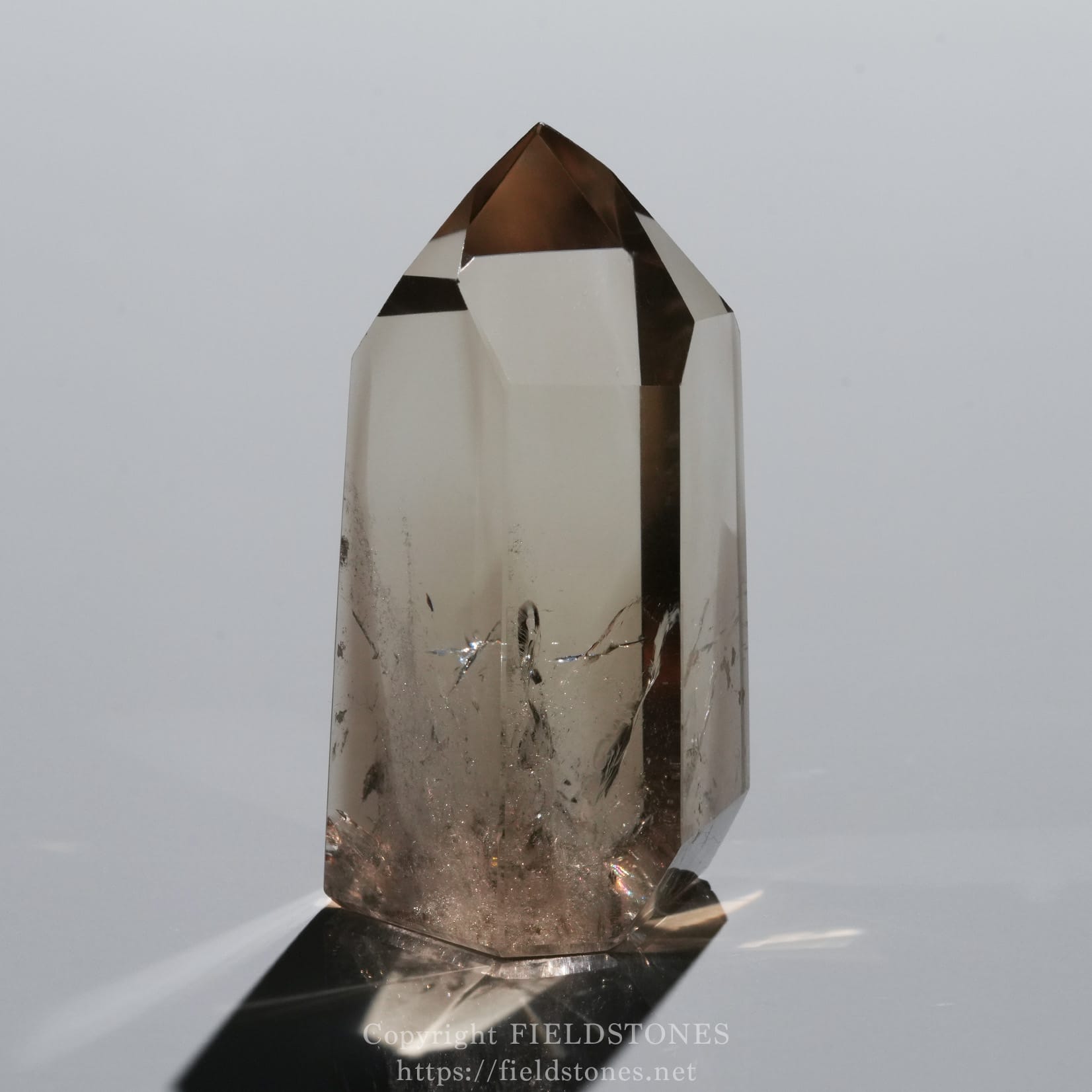 6709-6 - FieldStones Close-up of a clear quartz crystal point with a brown-tinted tip, showing multiple faceted surfaces and a reflective base.