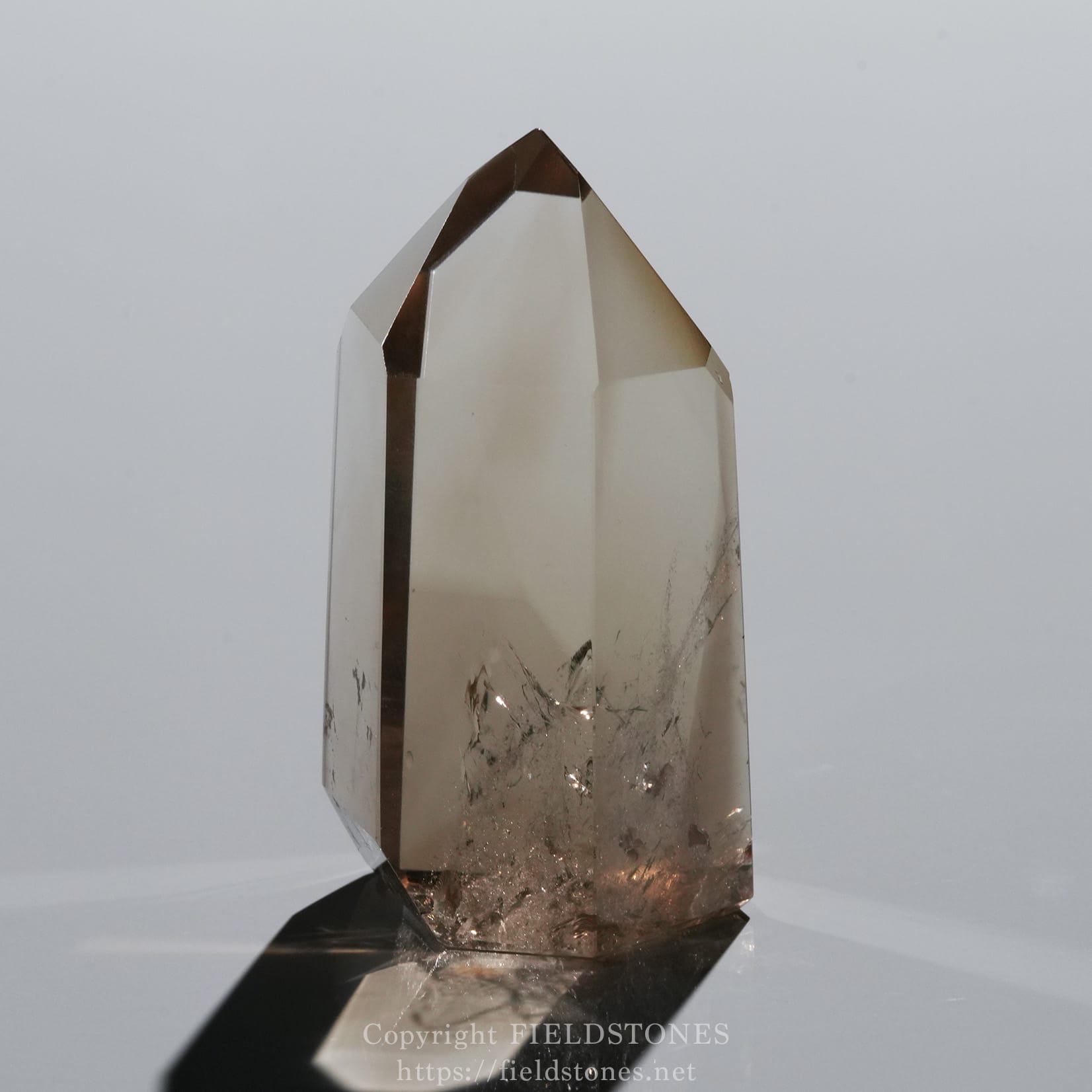 6709-8 - FieldStones Clear polished crystal obelisk with a pointed tip standing on a dark base, reflecting light.