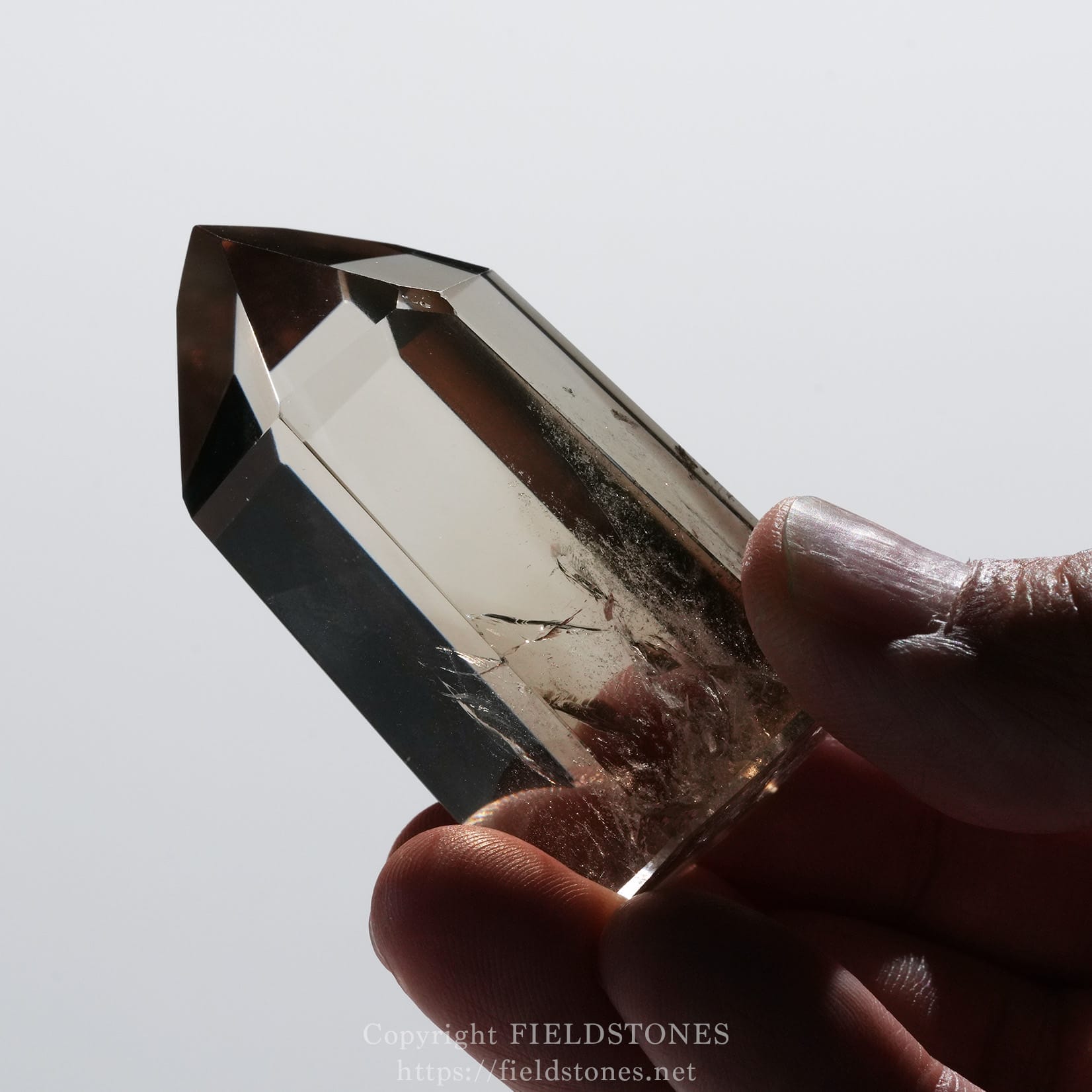 6709-9 - FieldStones Close-up of a faceted clear crystal being held between fingers.