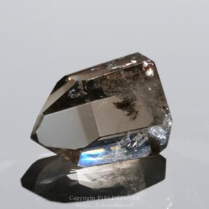 Close-up of a faceted smoky quartz crystal on a dark stand, reflecting on a glossy surface.
