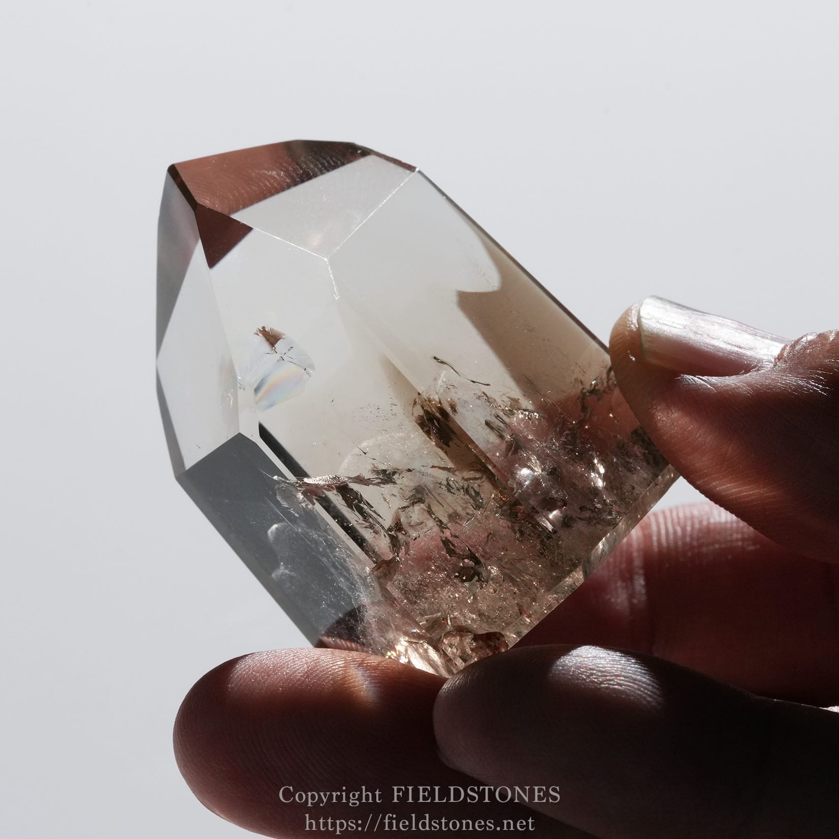 6710-10 - FieldStones Close-up of a clear faceted crystal being held between fingers.