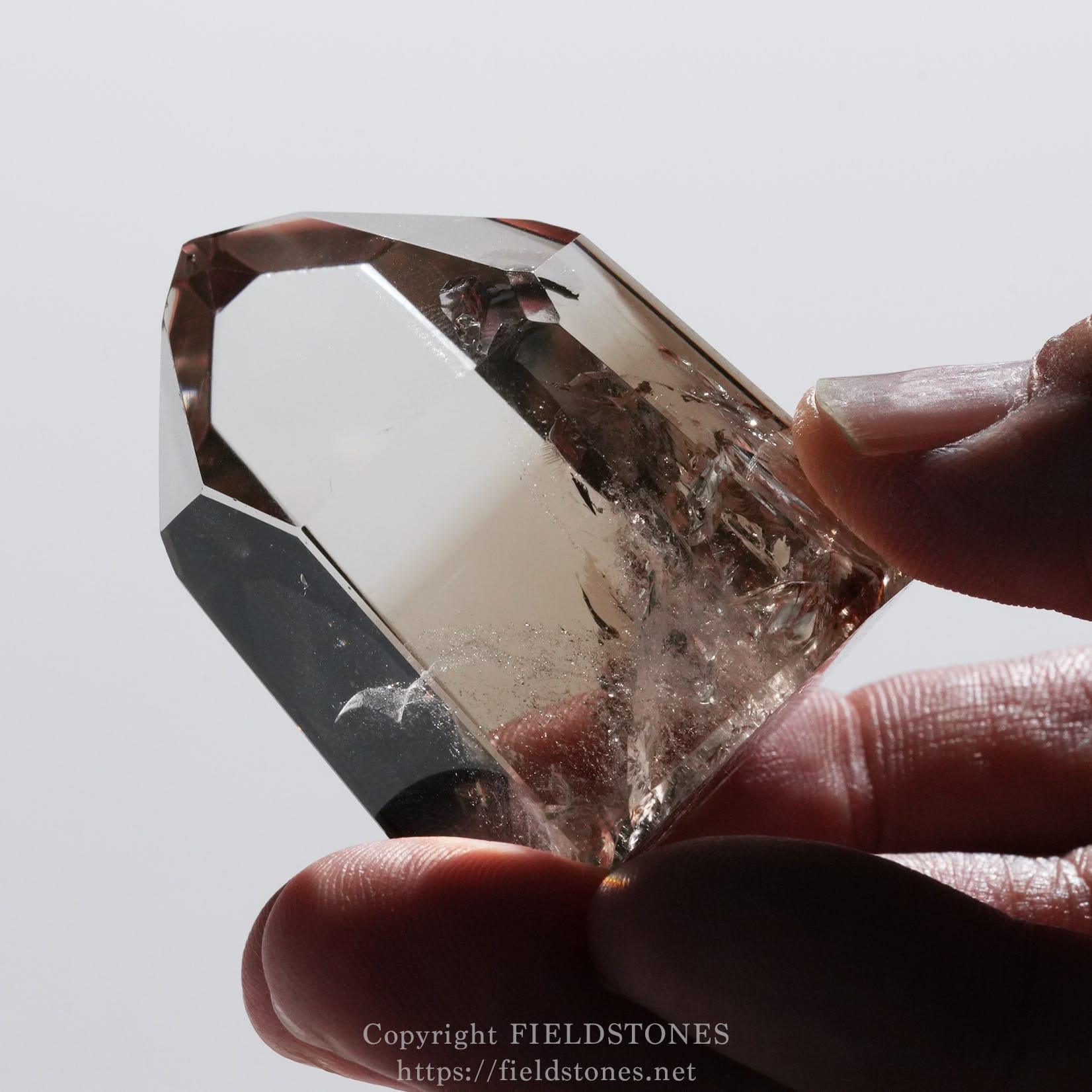 6710-11 - FieldStones Close-up of a faceted crystal gemstone held between thumb and index finger on a white background.