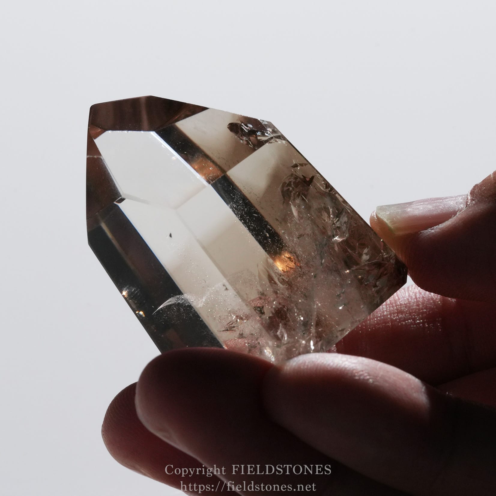 6710-12 - FieldStones Close-up of a faceted, transparent crystal held between fingertips by a person.