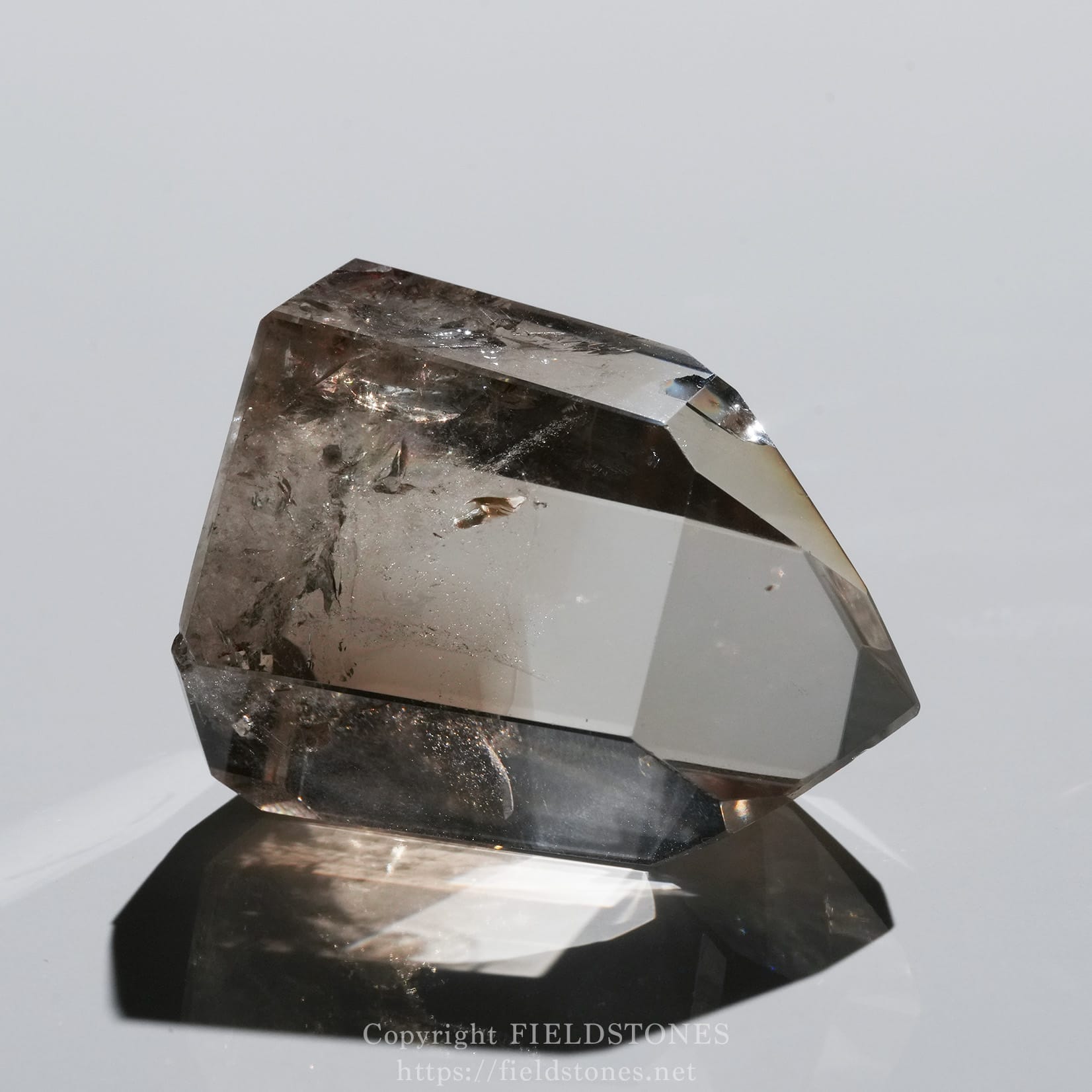 6710-2 - FieldStones Clear faceted crystal prism perched on a mirrored base, showing sharp edges and light reflections across its faces.