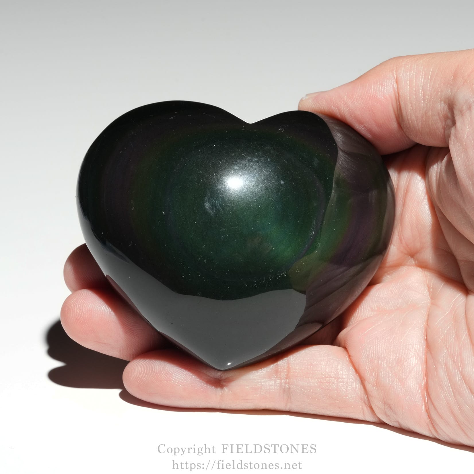 6711-4 - FieldStones Polished heart-shaped gemstone in dark green to black hues held between fingers.