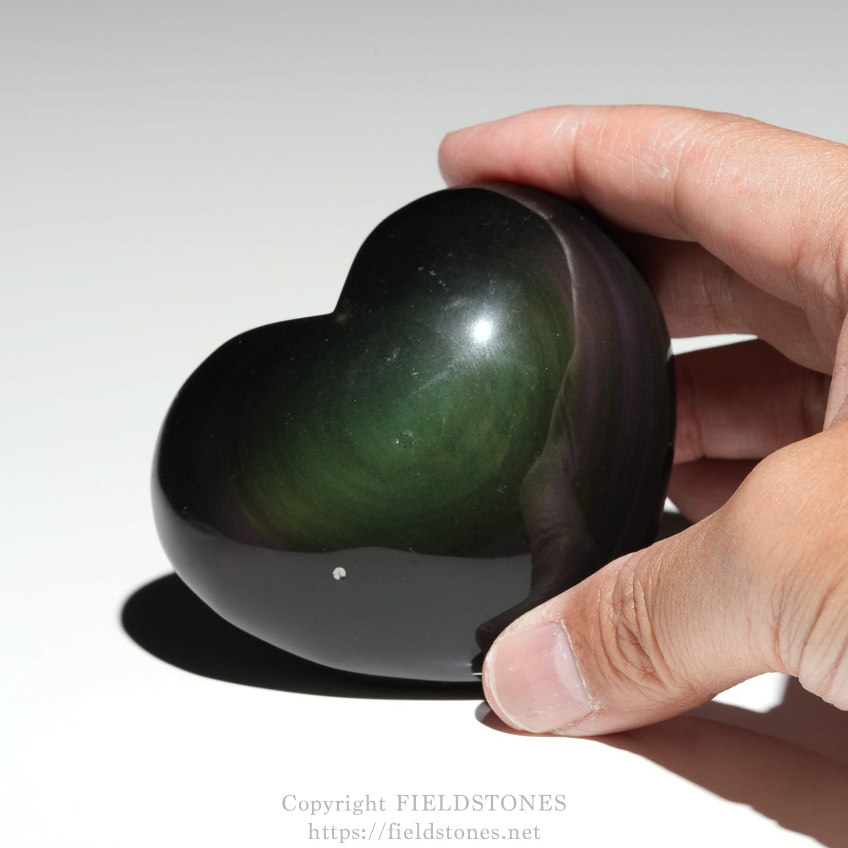 6711-7 - FieldStones Polished, dark green heart-shaped stone being held between fingers.
