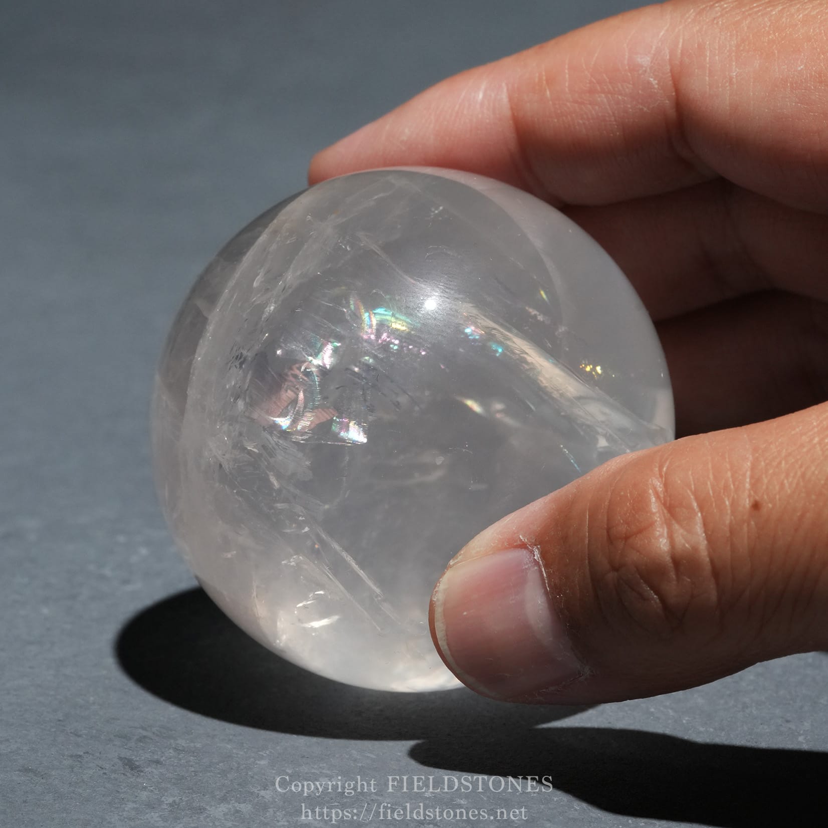 6719-3 - FieldStones Close-up of a hand pinching a translucent crystal sphere with rainbow reflections.
