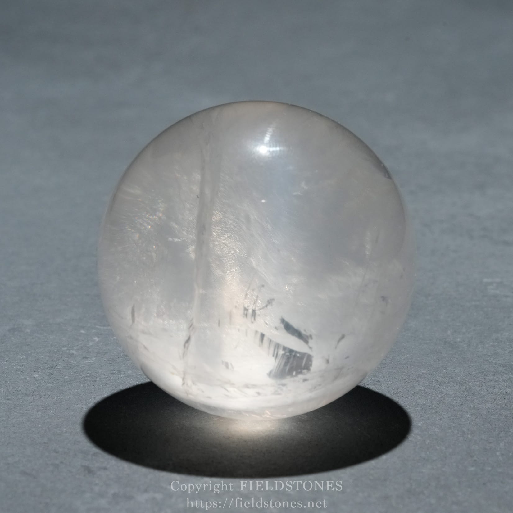 6719-8 - FieldStones Translucent white crystal sphere resting on a dark surface with a soft shadow beneath it.