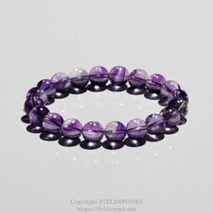 Purple glass bead bracelet arranged in a circle on a reflective surface with soft highlights.