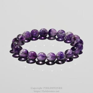 Purple gemstone bead bracelet arranged in a near-circle on a reflective surface, with soft reflections underneath.