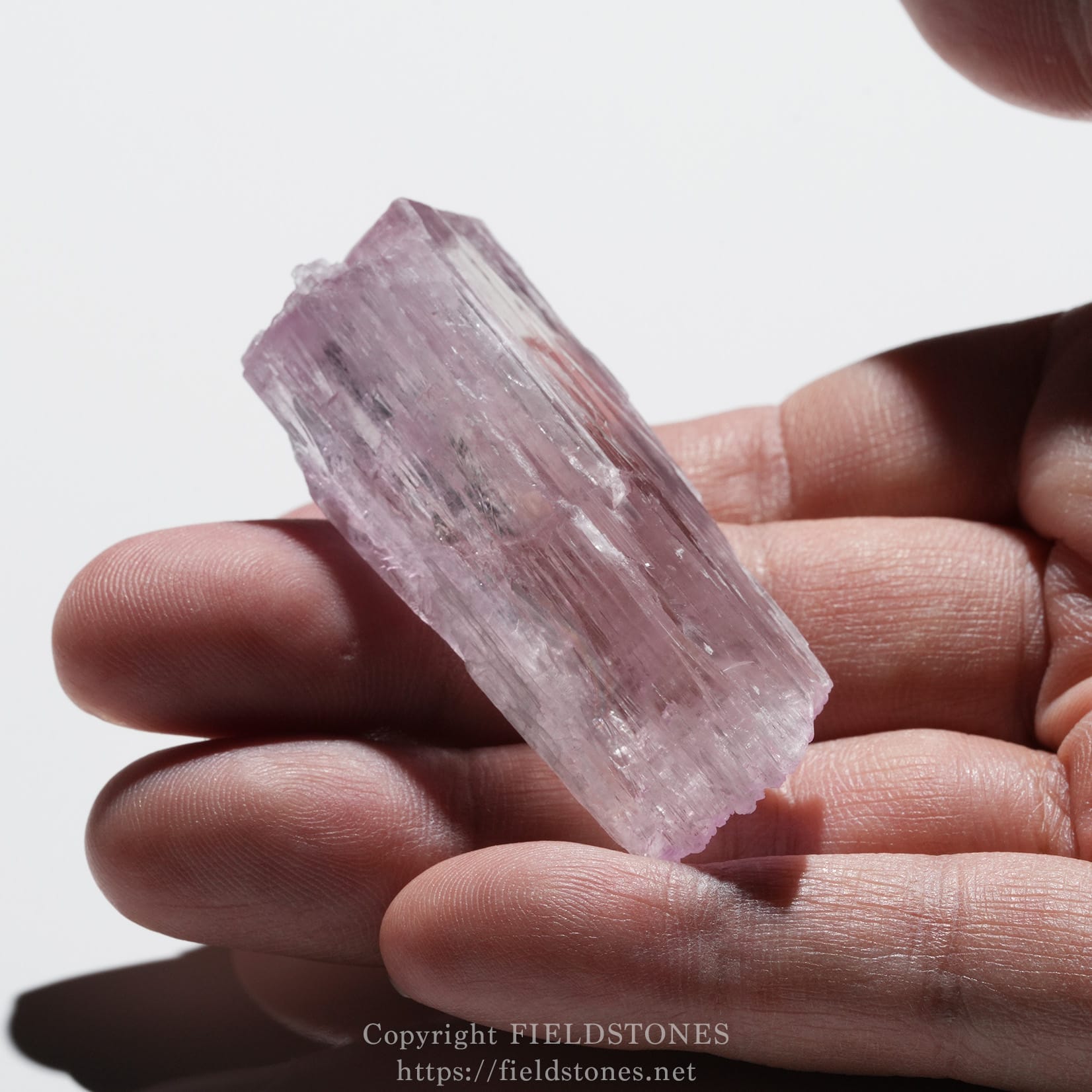 6726-12 - FieldStones Hand holding a rough, translucent pink crystal with visible striations between the fingers