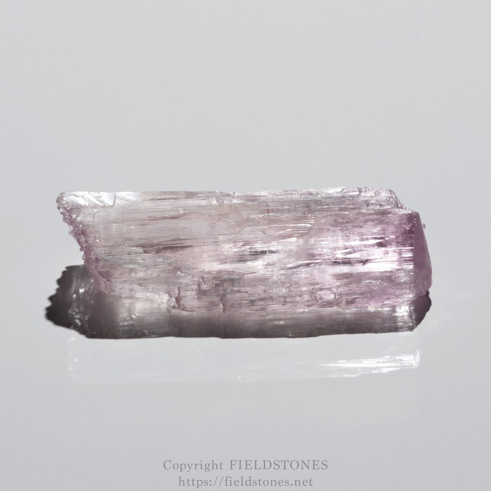 6726-2 - FieldStones Rectangular pink kunzite crystal with rough facets resting on a light gray surface.