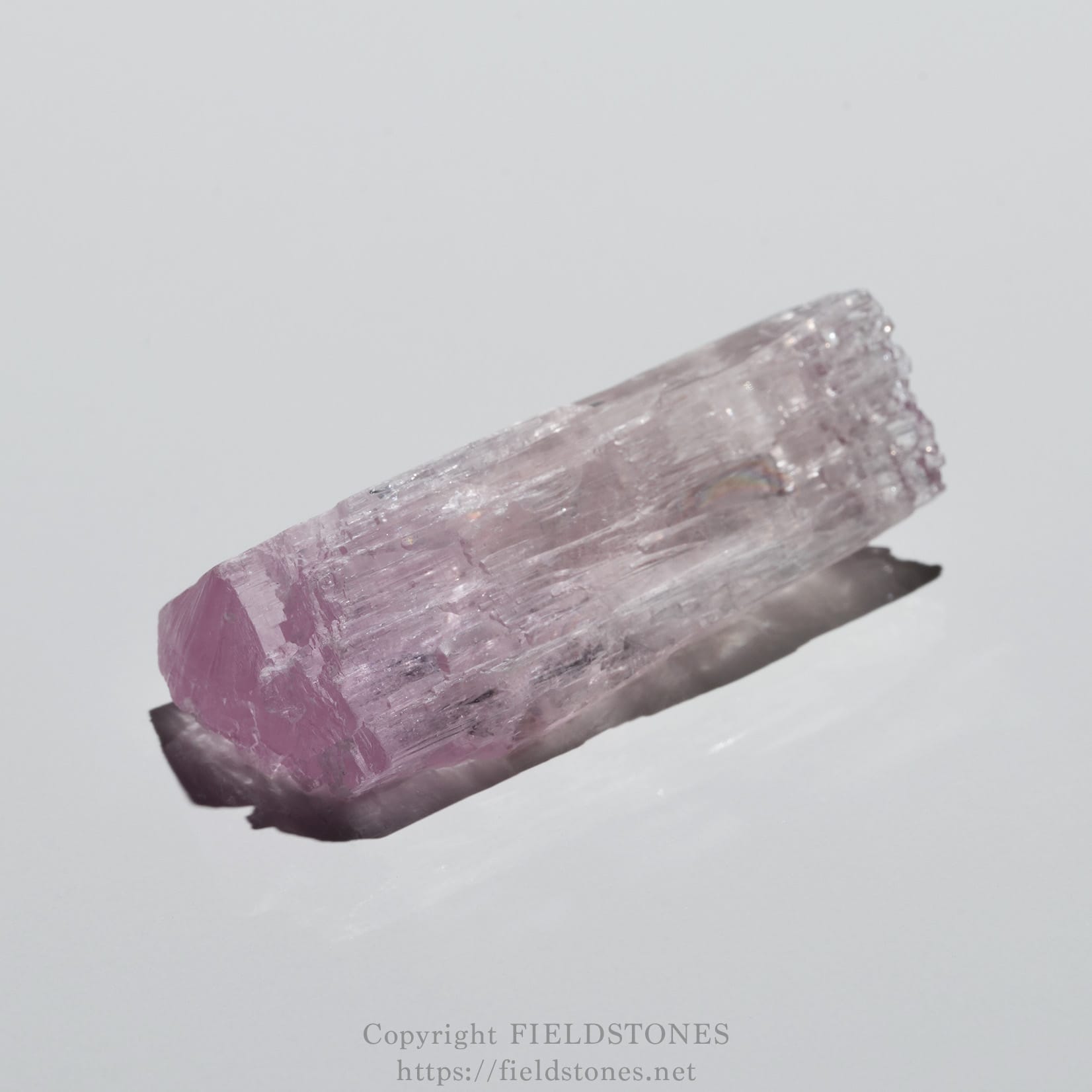 6726-4 - FieldStones Close-up of a pink-purple prismatic crystal with rough facets against a pale background.