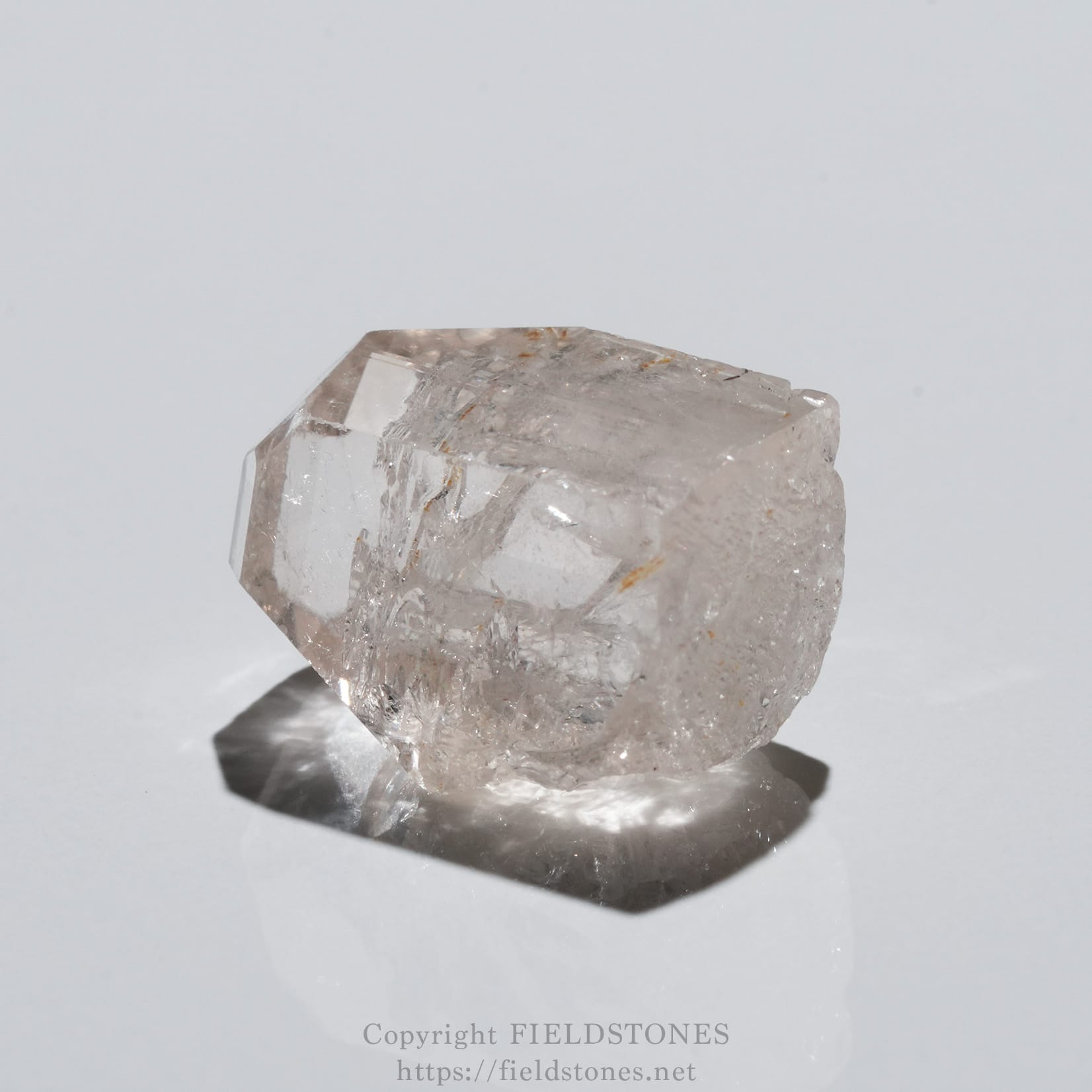 6737-10 - FieldStones Clear translucent quartz crystal resting on a white surface, showing faceted edges and natural imperfections.