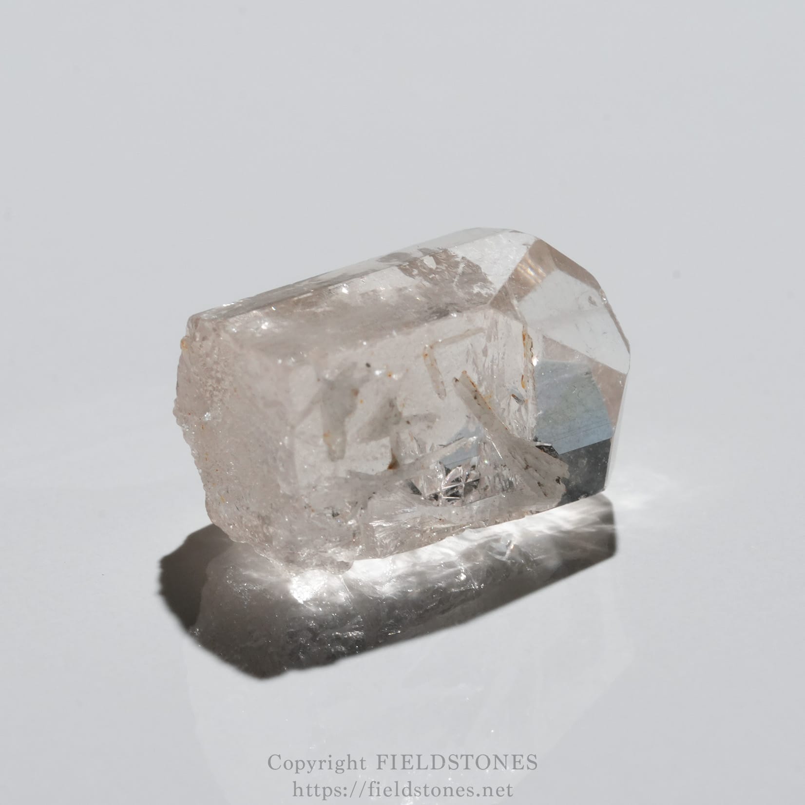 6737-11 - FieldStones Close-up of a translucent quartz crystal on a white surface with subtle reflections.