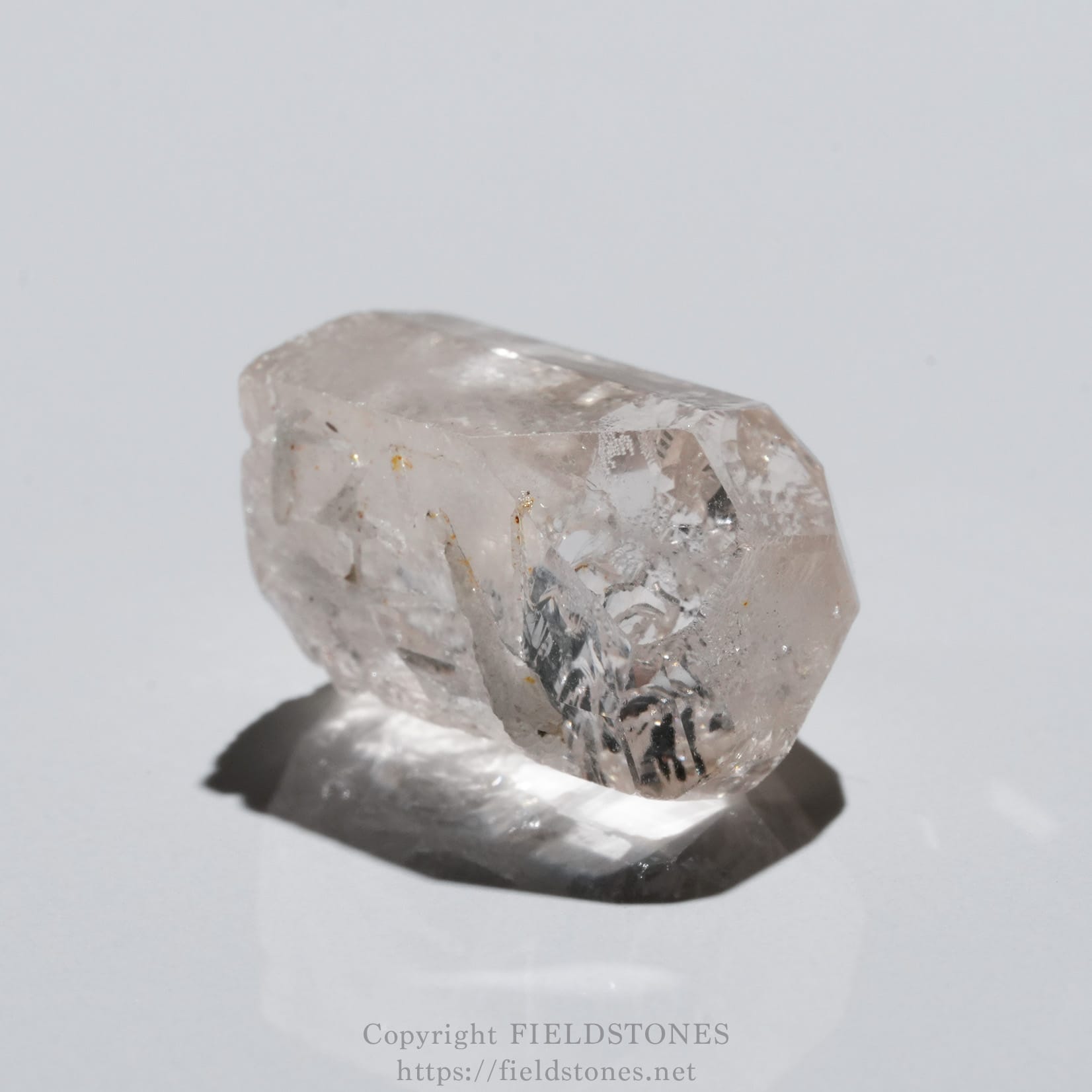 6737-12 - FieldStones Close-up of a translucent quartz crystal with pointed facets on a white background (watermarked)