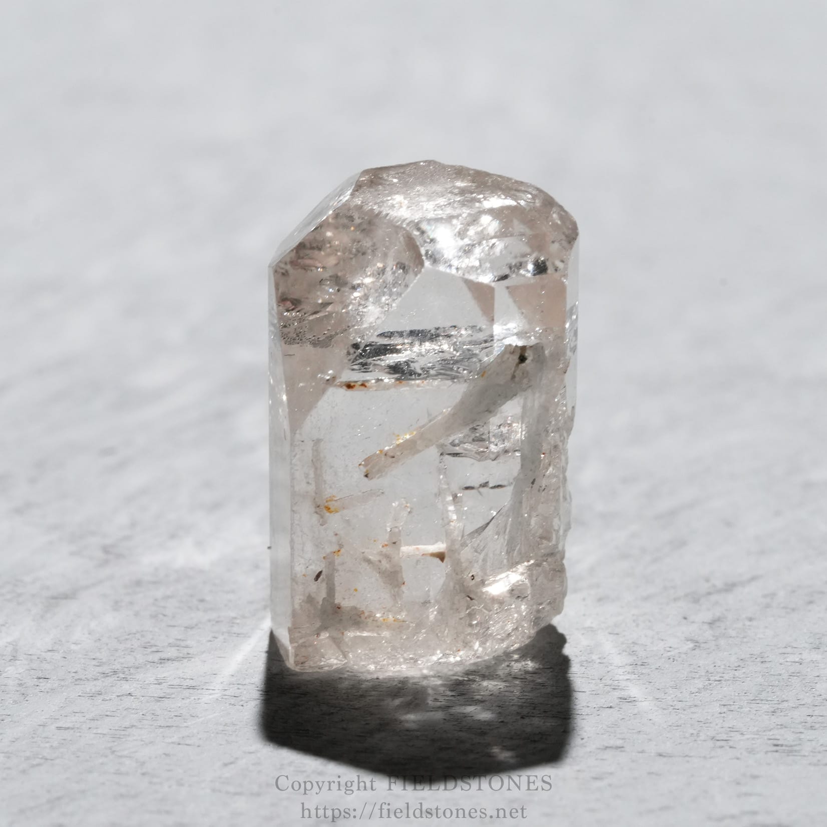 6737-3 - FieldStones Close-up of a clear quartz crystal standing upright on a gray textured surface.