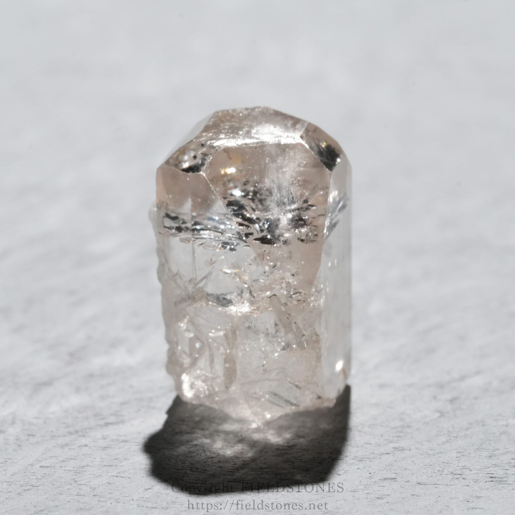 6737-5 - FieldStones Close-up of a translucent quartz crystal with a faceted tip, standing upright on a gray surface.