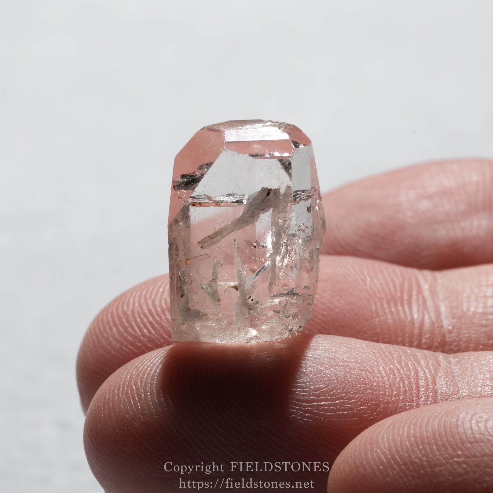 6737-7 - FieldStones Small pink rose quartz crystal held between fingertips with a light, translucent surface.