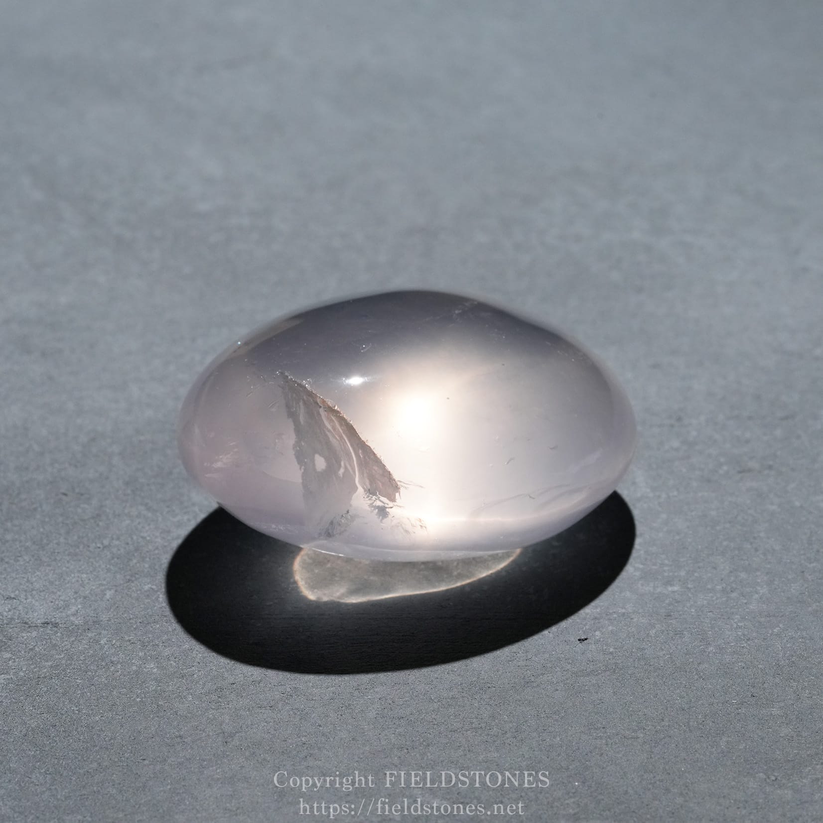 6740-11 - FieldStones Polished gray pebble with a white streak resting on a dark surface, casting a shadow.