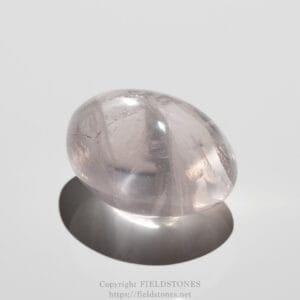 Polished rose quartz stone resting on a white surface with a soft shadow beneath it.
