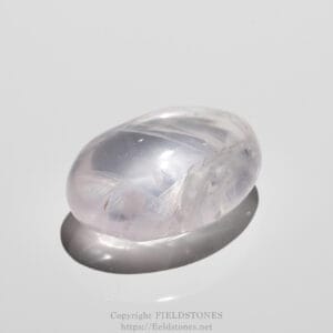 Close-up of a smooth, translucent lavender gemstone (amethyst) on a light surface with a soft reflection.