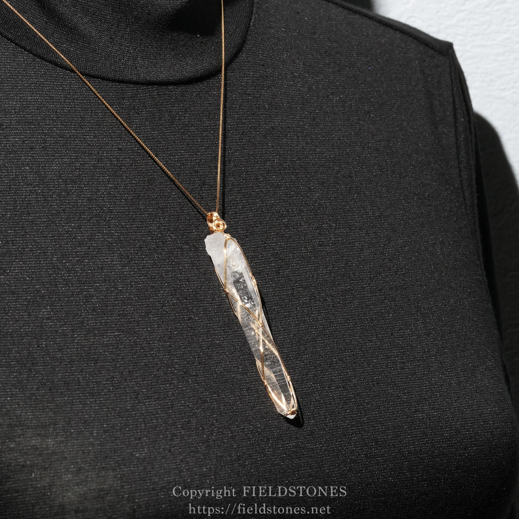 6751-11 - FieldStones Gold necklace with a raw crystal pendant wrapped in gold wire, resting on dark fabric background.