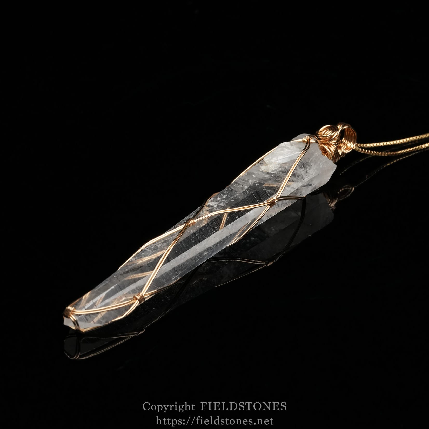 6751-3 - FieldStones Clear quartz crystal pendant wrapped in copper wire on a black reflective surface.