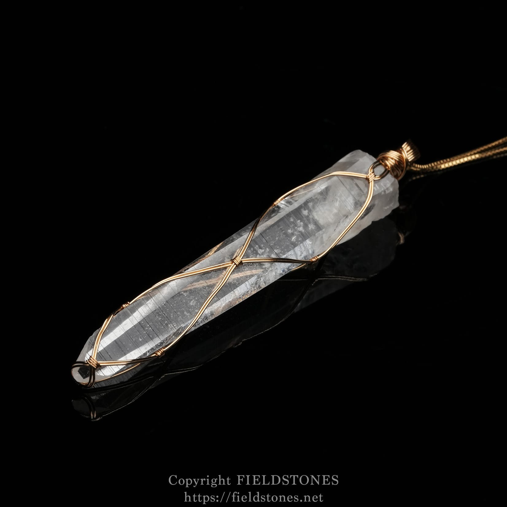 6751-5 - FieldStones Close-up of a clear quartz crystal pendant wrapped in copper wire on a black reflective surface.
