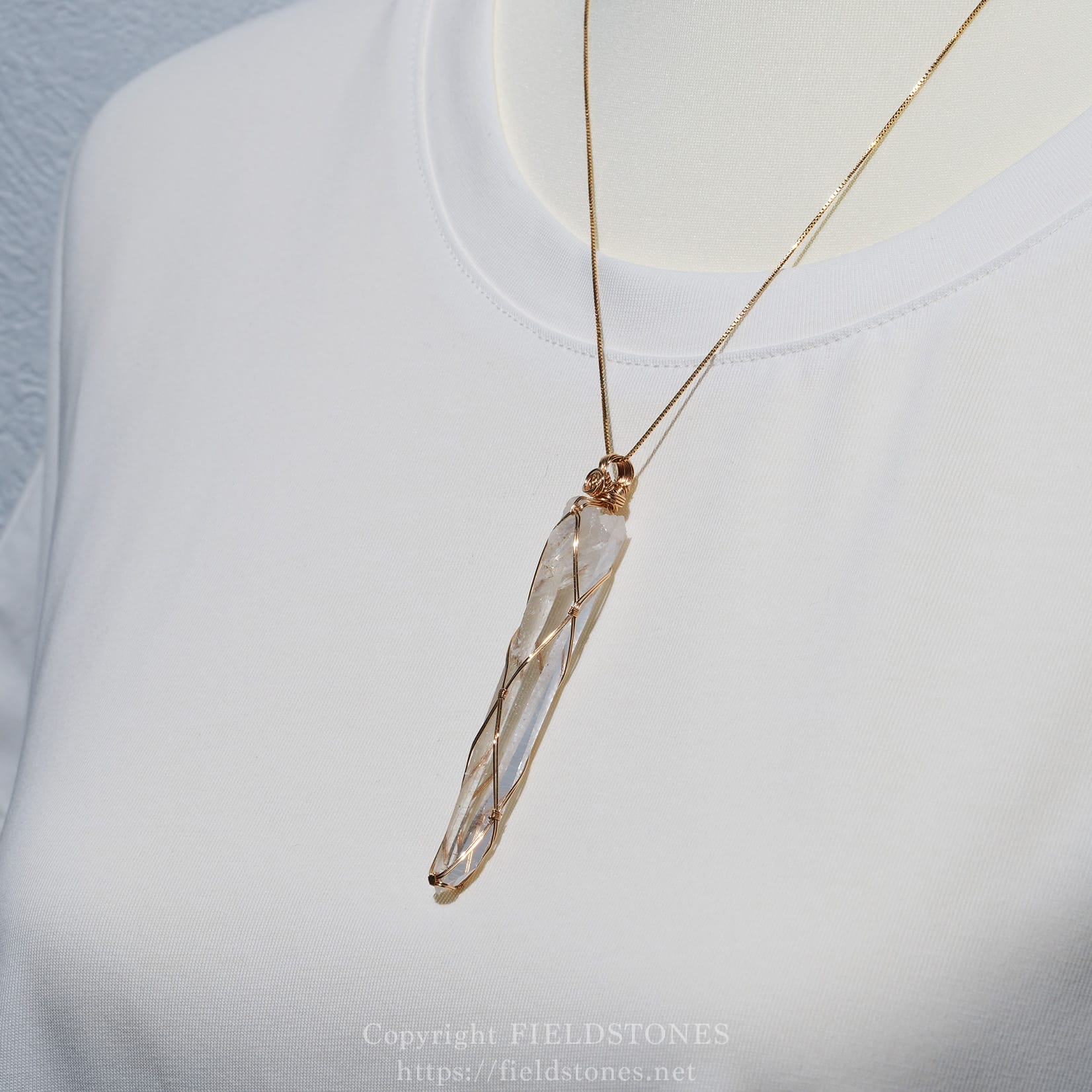 6751-6 - FieldStones Gold chain with a wire-wrapped crystal pendant resting on a white shirt near the neckline