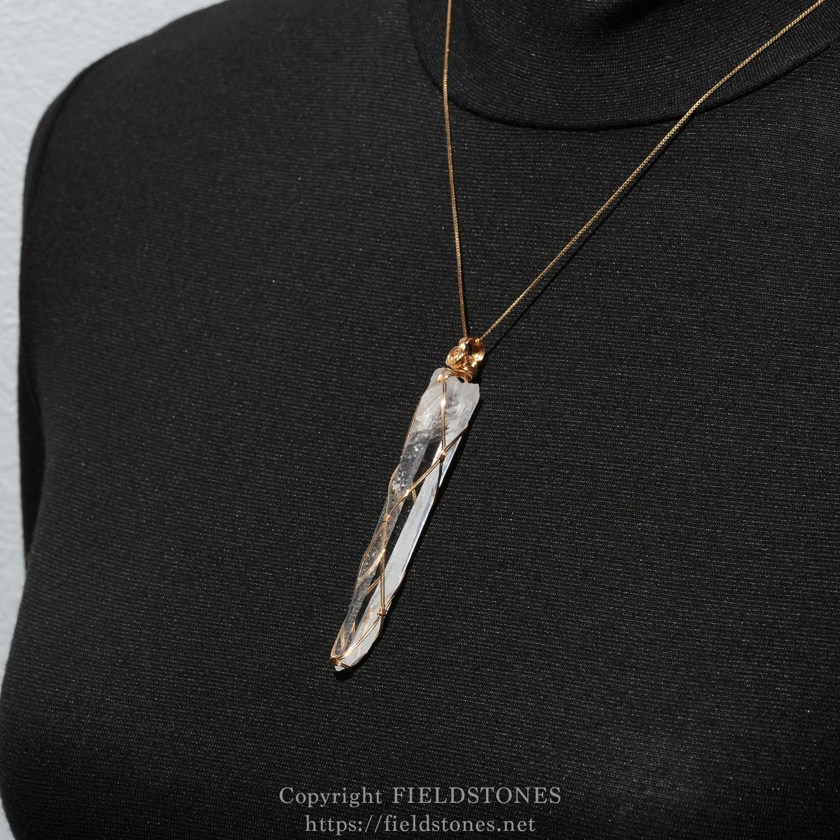 6751-9 - FieldStones Crystal pendant wrapped in gold wire on a thin gold chain against a black turtleneck fabric.