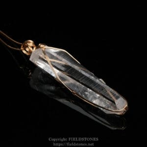 Crystal quartz pendant wrapped in copper wire on a black background, close-up jewelry shot