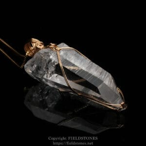 Copper-wrapped quartz crystal pendant on a dark background, with delicate wire coils encircling the crystal edge and forming a loop for a chain