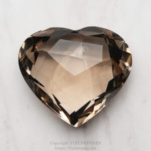 Heart-shaped, faceted smoky quartz gemstone resting on a pale marble surface