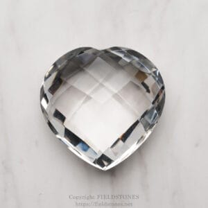 Heart-shaped faceted crystal on a light marble surface, reflecting light in geometric facets.