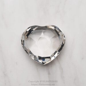 Faceted crystal heart resting on a light marble surface, catching subtle light reflections.
