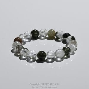 Bracelet made of round translucent gemstone beads with internal inclusions, arranged in a circle on a glossy white surface with reflections.